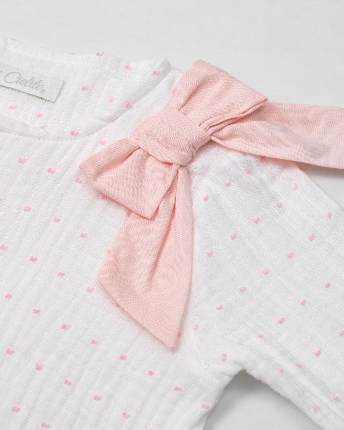 Pijama enteriza blanca con puntitos rosados, detalle de moño y botones para bebé niña