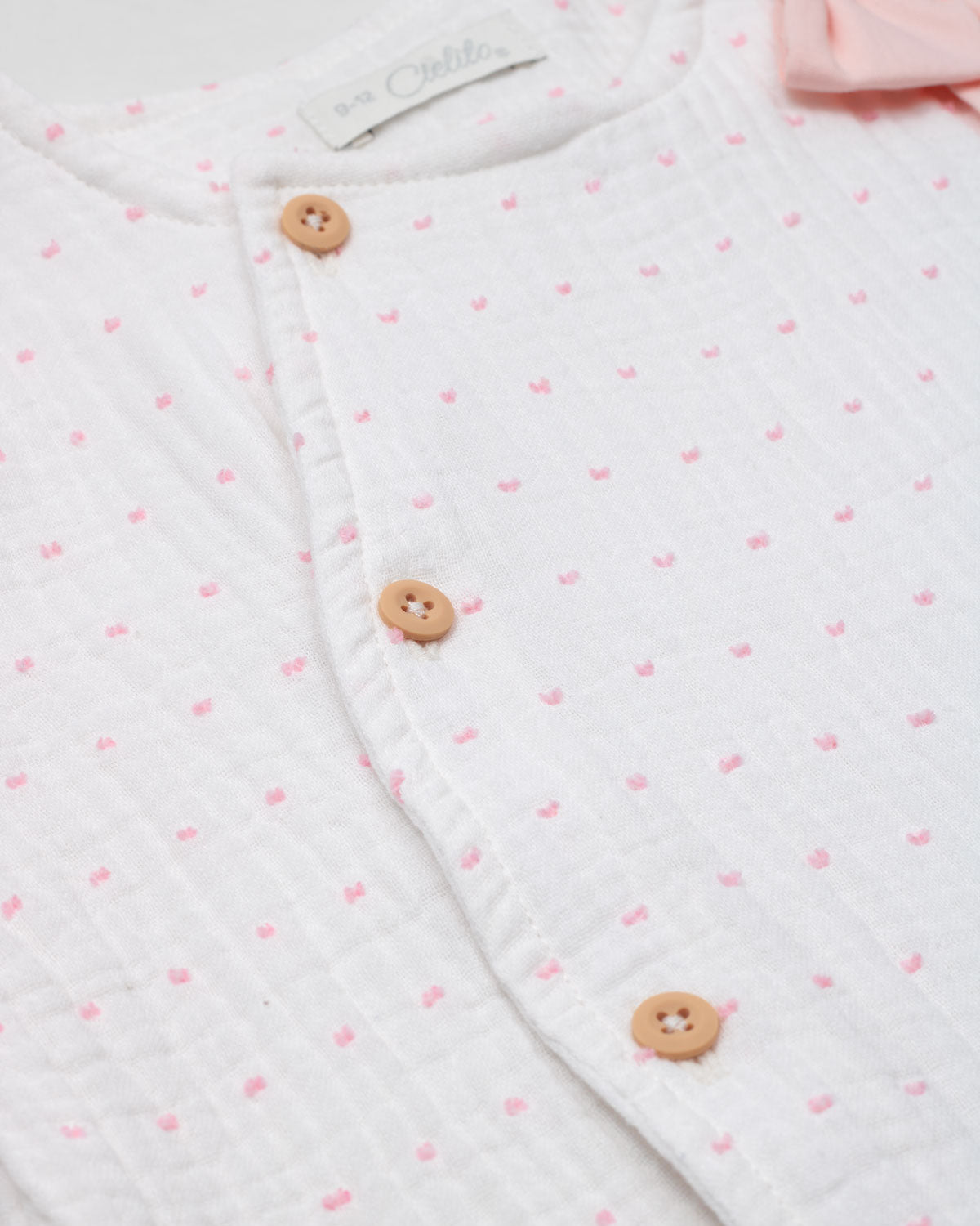 Pijama enteriza blanca con puntitos rosados, detalle de moño y botones para bebé niña