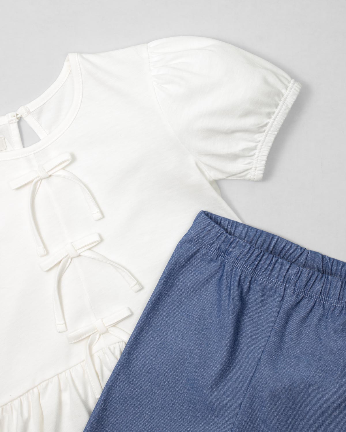 Conjunto blusa blanca con detalle de moñitos, terminado en bolero y leggins azul para niña