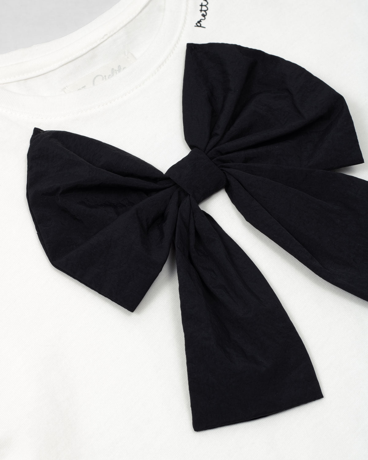 Camiseta con aplique moño en negro y estampado en cuello para niña