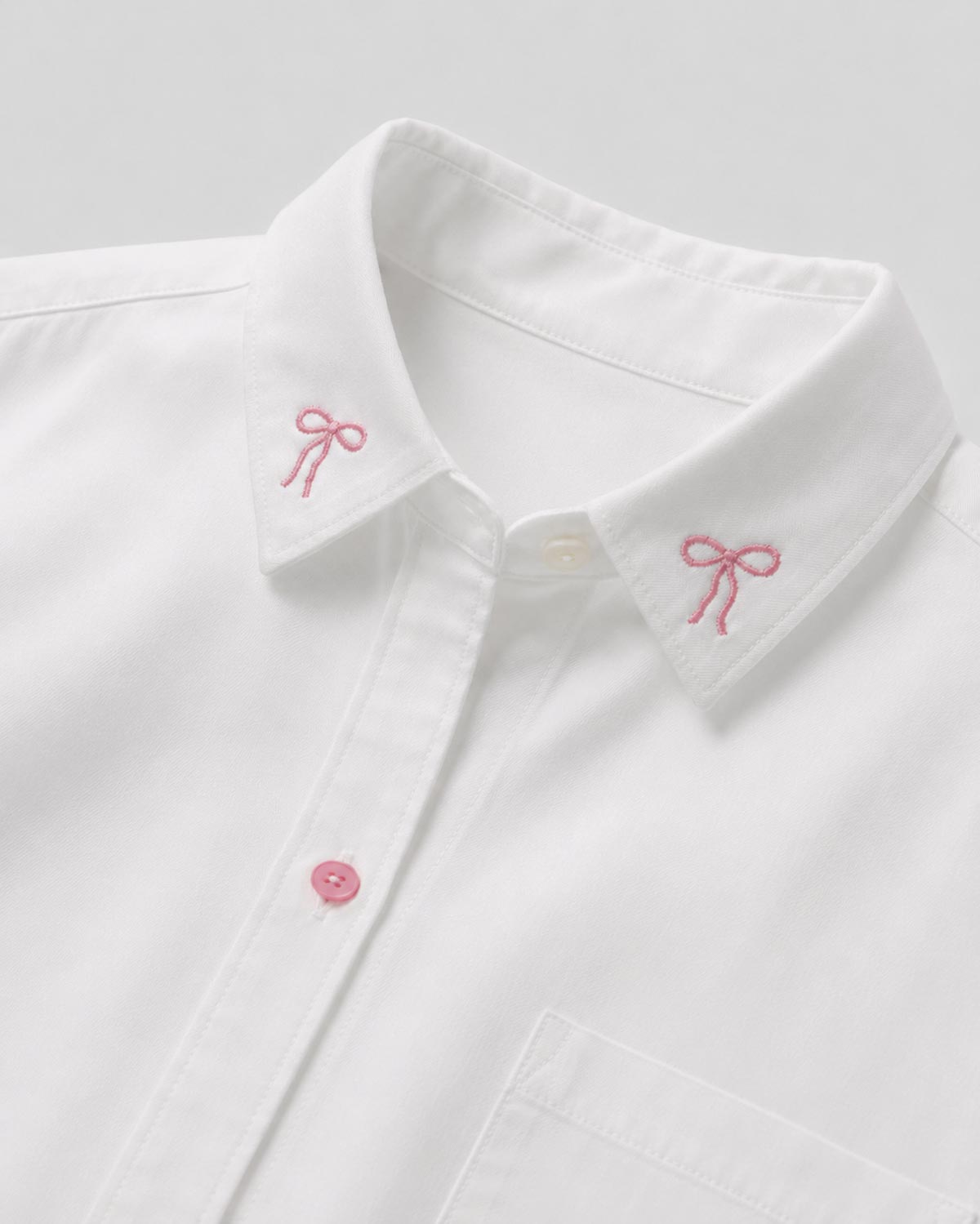 Camisa blanca con pequeño bordado de moños y bolsillo para niña