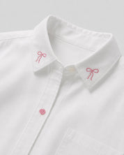 Camisa blanca con pequeño bordado de moños y bolsillo para niña