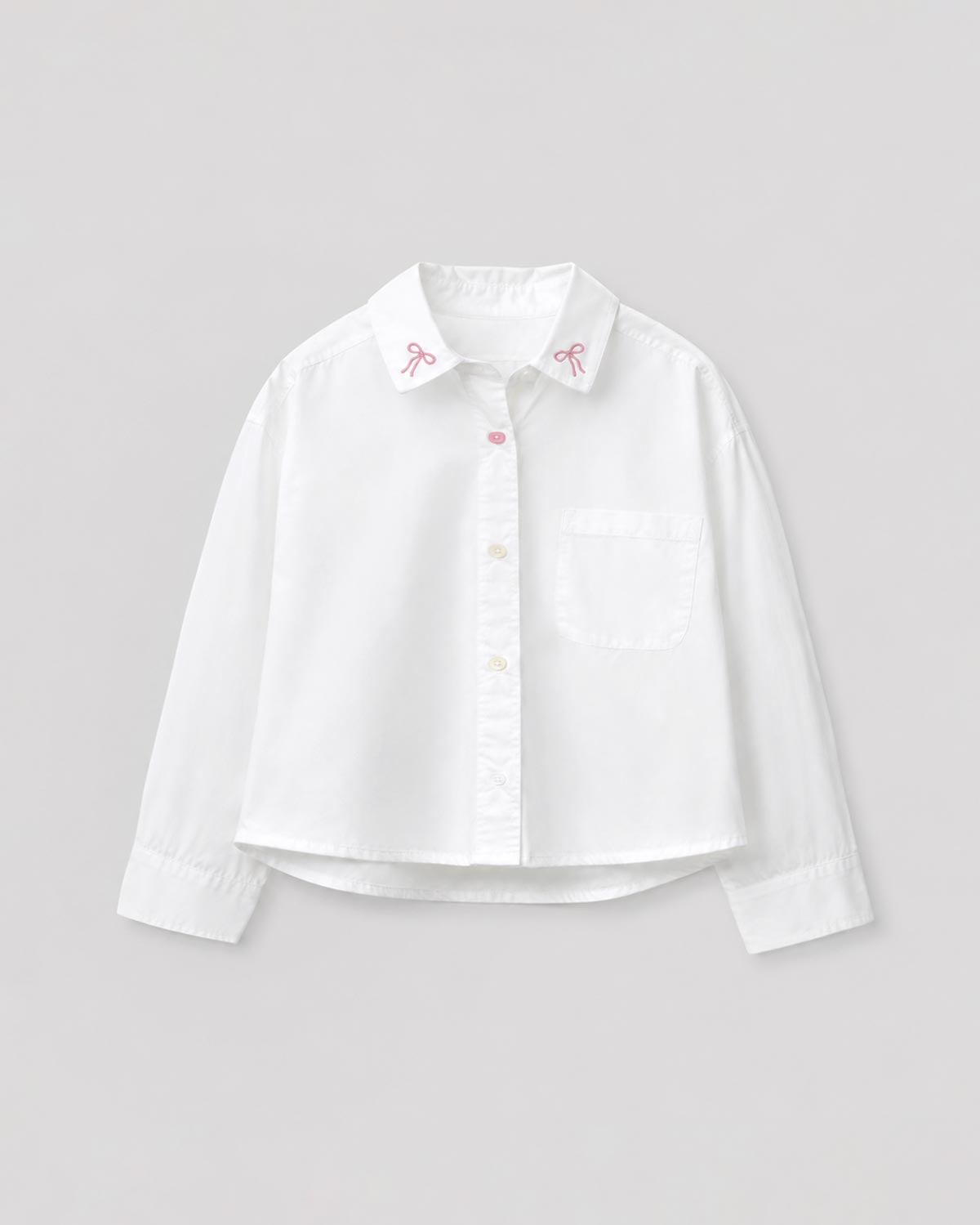 Camisa blanca con pequeño bordado de moños y bolsillo para niña