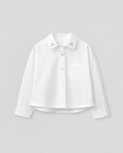 Camisa blanca con pequeño bordado de moños y bolsillo para niña